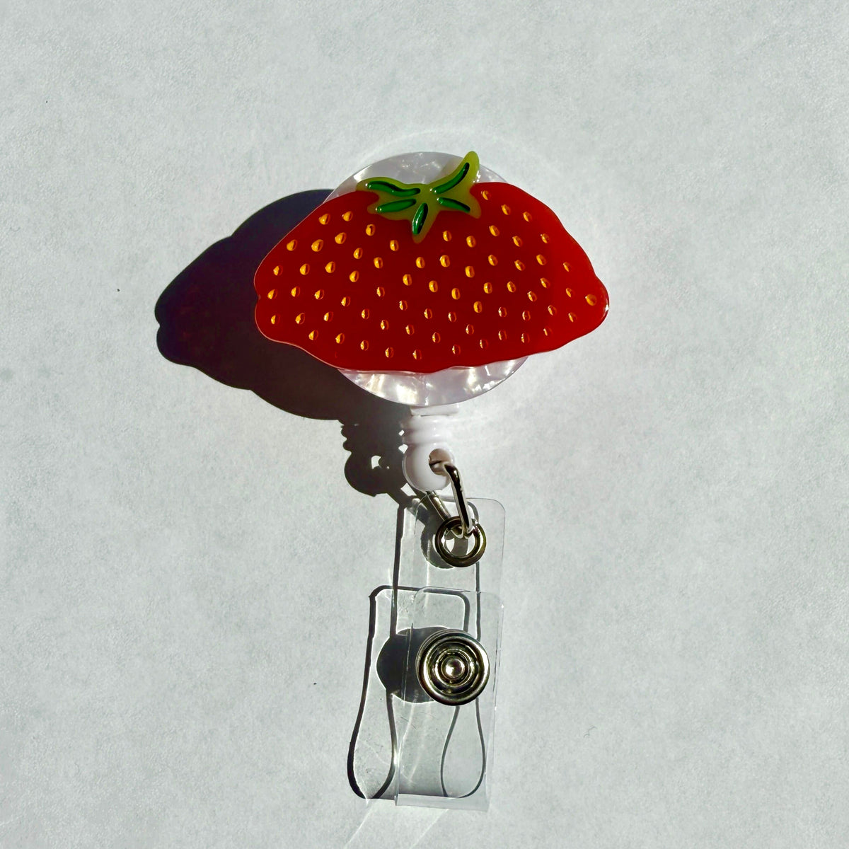 The Megaberry Badge Reel from the front on a plain white background, showing the red strawberry with yellow seeds on a white pearl reel and the clear badge strap.