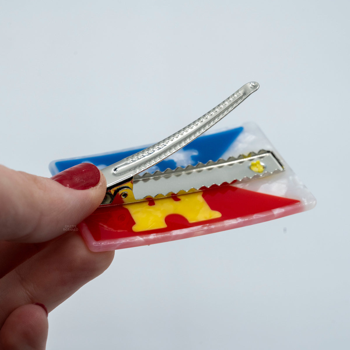 A persons hand holding an acadiana flag hair clip with the clip opened
