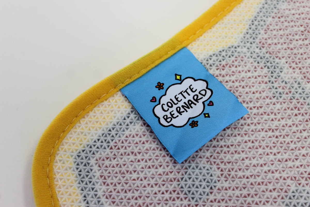 A close up of the blue Colette Bernard tag sewn onto the back of the Crawfish Claw Rug, next to its yellow edge binding.
