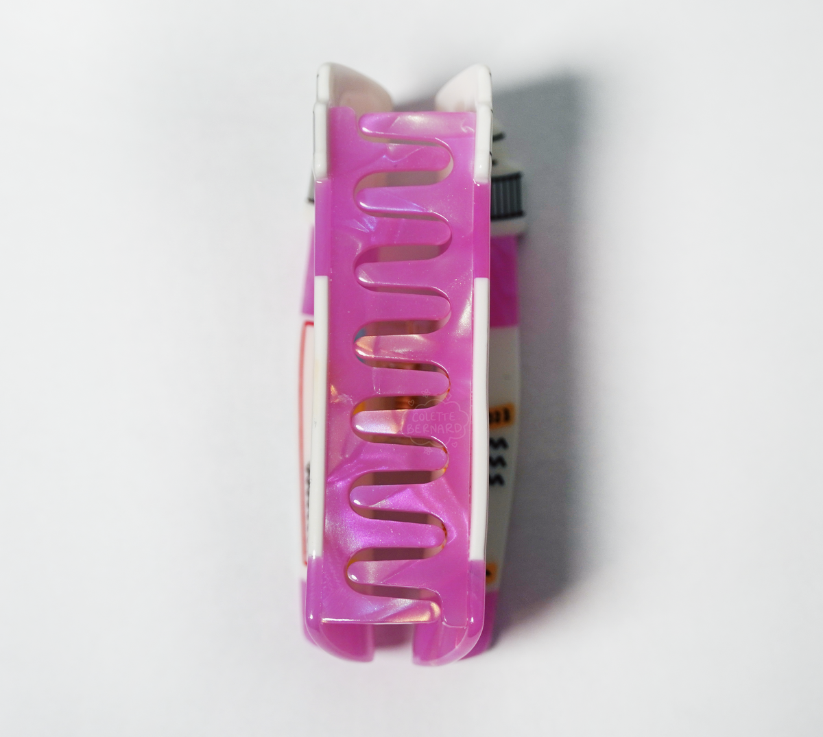 The Pink Prescription Bottle Hair Claw viewed from the side on a white background, showing the interlocking pink teeth of the claw.