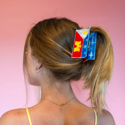 A woman shown from the back wearing a hair claw featuring the design of the acadiana flag. 