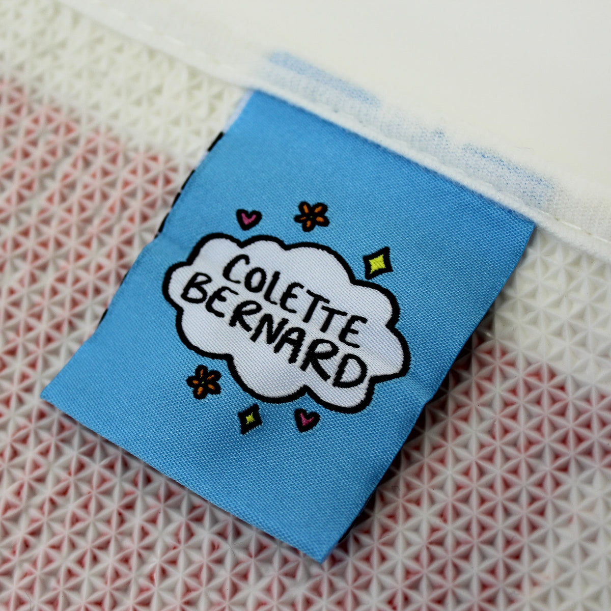close up of the tag on the rug. The tag is blue with the Artist Colette logo