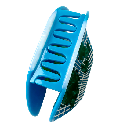 The World Map Hair Claw from the side, showing the blue teeth of the claw and the green and white grid map pattern on the outer face.