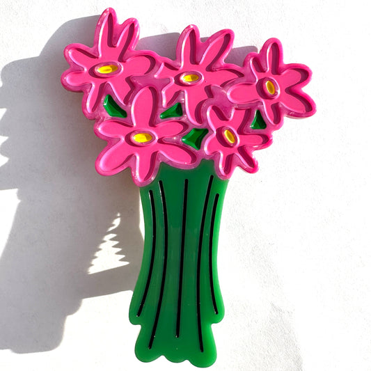 A colorful flower bouquet hair clip featuring bright pink daisy-like flowers with yellow centers and a green stem, photographed against a white background 