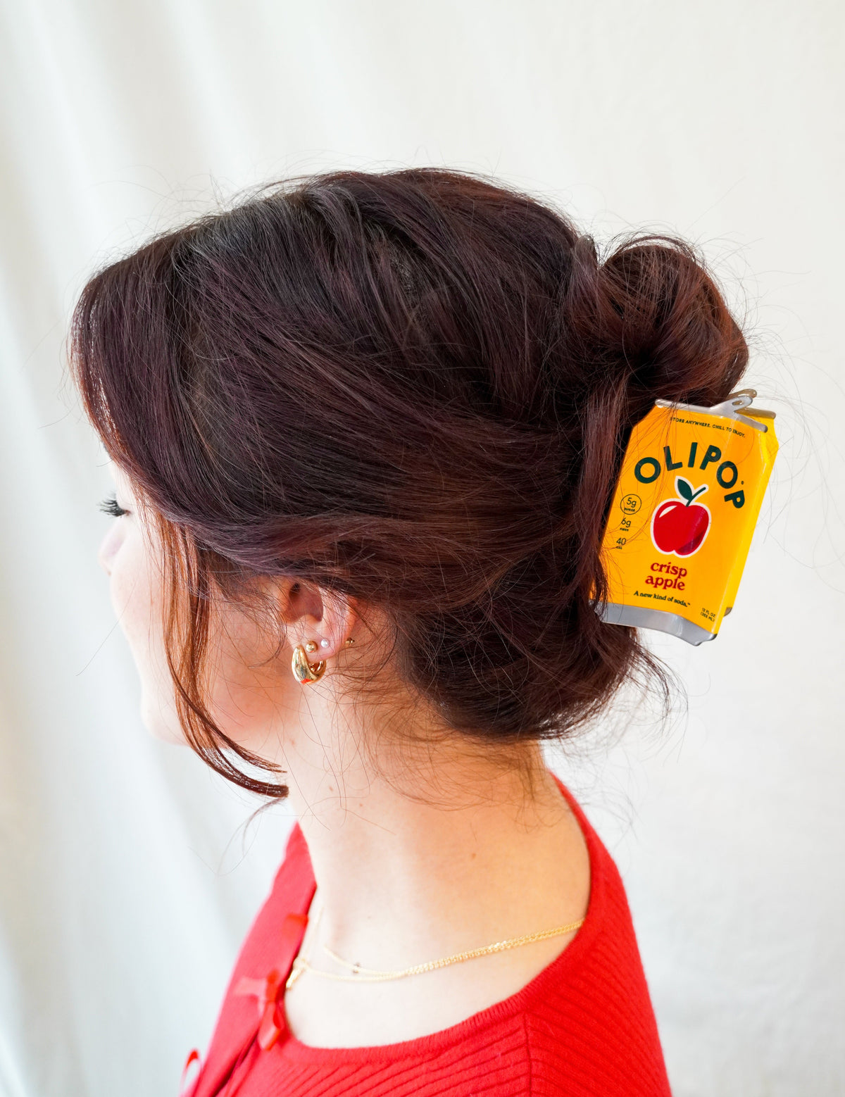 A woman with dark brown hair in a bun wears a yellow Olipop Crisp Apple hair claw. 