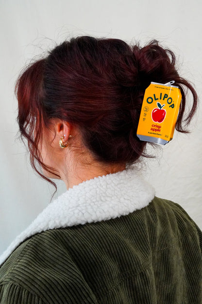 A person shown from the back wearing a dark olive green corduroy jacket with a white sherpa collar, with their hair in a bun secured by a OLIPOP Crisp Apple Hair Claw