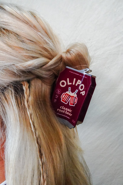 A close-up of a person's blonde hair styled in a half-up bun with a OLIPOP Classic Root Beer hair claw clipped into the hair 