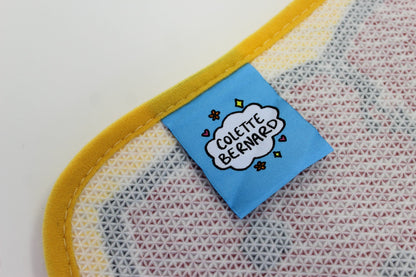 A close up of the blue Colette Bernard tag sewn onto the back of the Crawfish Claw Rug, next to its yellow edge binding.