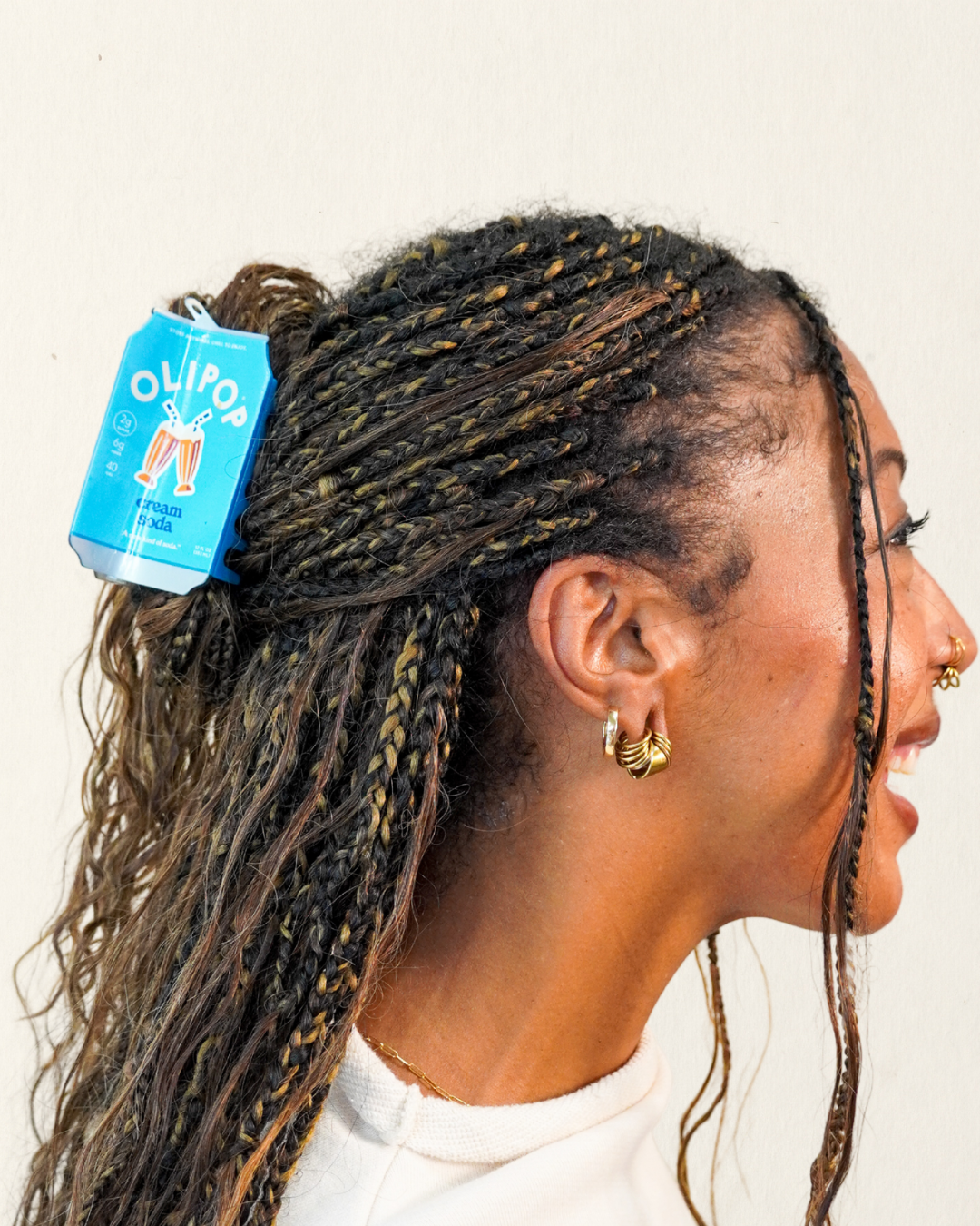 A close-up side profile of a person with long braided hair, wearing a Olipop cream soda hair claw in their hair, half up