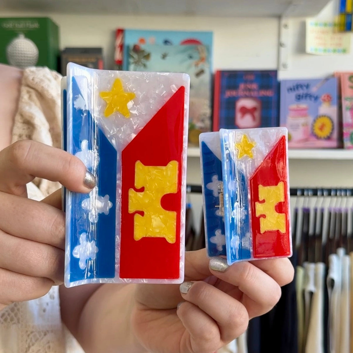 a person holding an acadiana flag mega claw and an acadiana flag hair claw next to each other