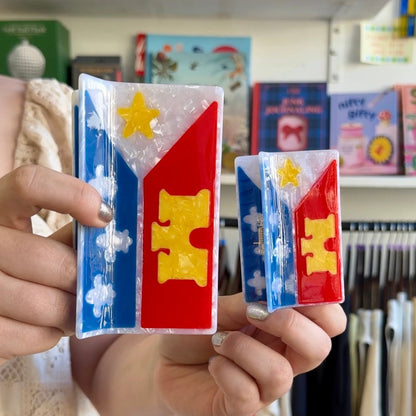a person holding an acadiana flag mega claw and an acadiana flag hair claw next to each other