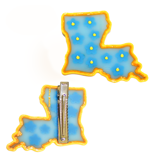 The Louisiana State Clip shown front and back, shaped like the state of Louisiana in blue with a yellow edge and blue flowers with yellow centres, with the silver alligator clip on the back.