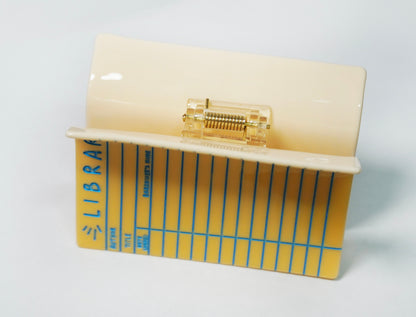 The Library Card Hair Claw viewed from the back, showing the spring mechanism and the cream back of the claw, on a white background.