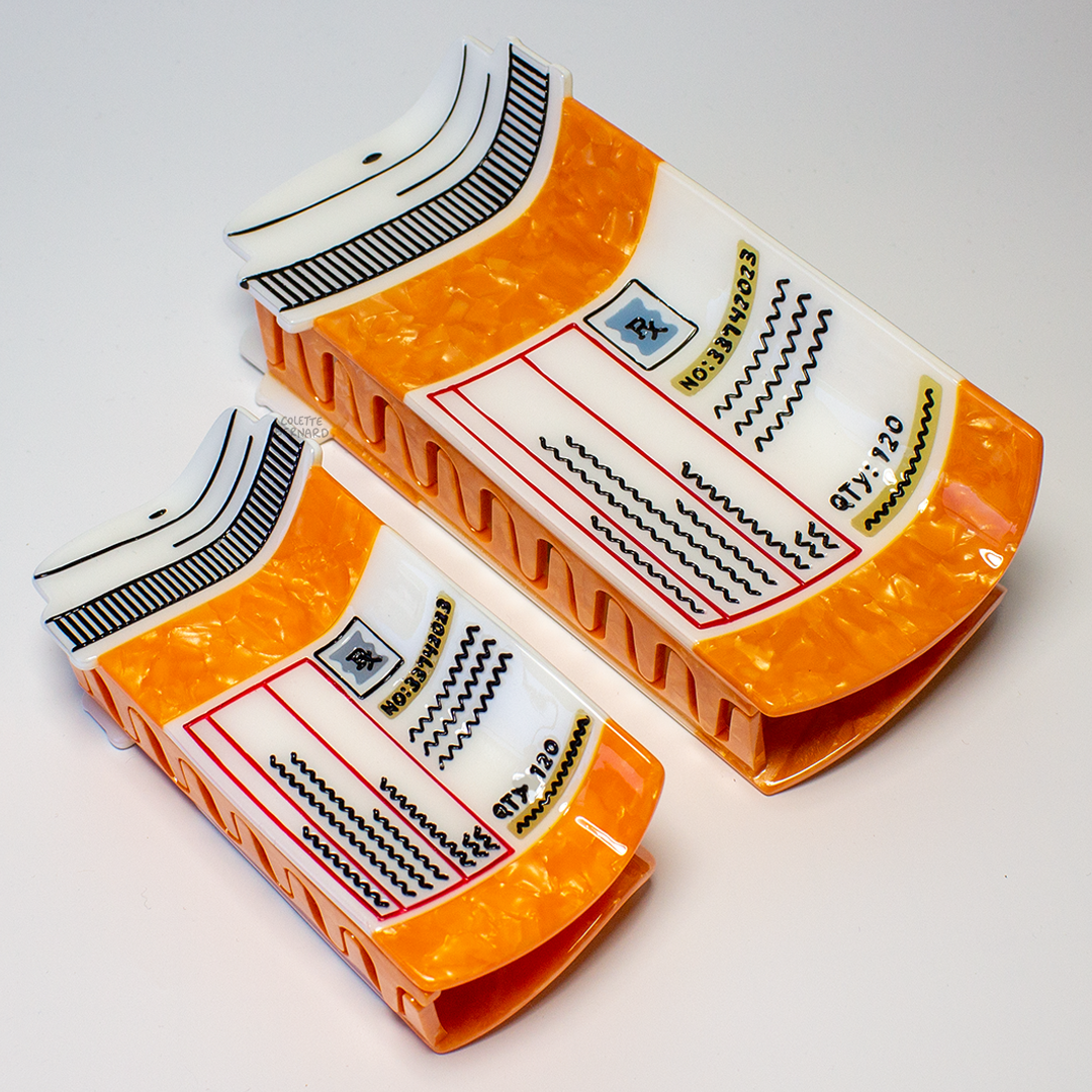 The Prescription Bottle Mega Claw and the standard size Prescription Bottle Hair Claw lying on their sides to show the size difference, with the teeth of the claws visible.