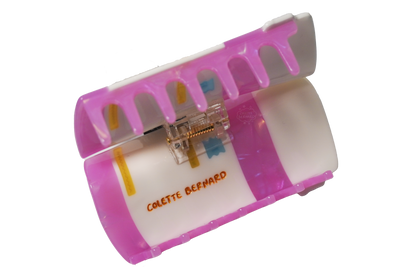 The Pink Prescription Bottle Hair Claw held open on a white background, showing the pink teeth, the spring mechanism and the orange Colette Bernard logo.