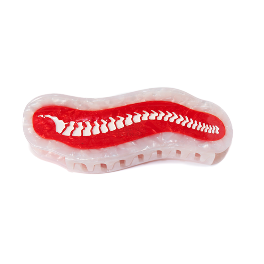 The Spine Claw, a white pearl hair claw with a red marbled centre and a white spine of vertebrae running along it, on a white background.