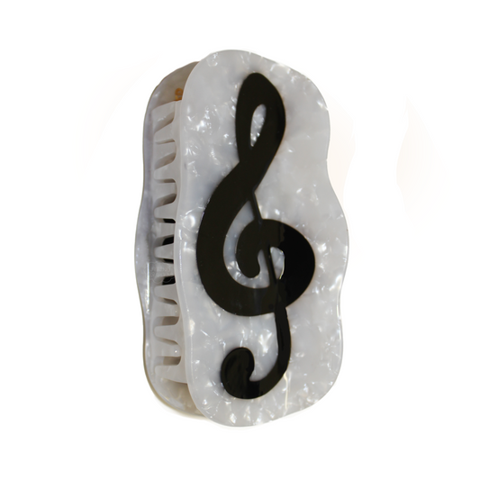 A white pearl hair claw with a black treble clef on the front, shown at an angle with the teeth visible, on a plain white background.